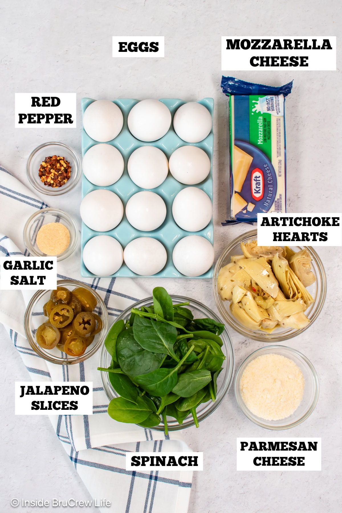 A white board with bowls of ingredients needed to make an egg casserole with spinach and cheese.