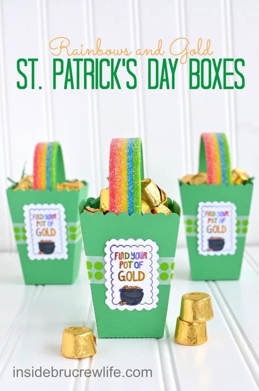 St. Patrick's Day Boxes - easy paper boxes filled with chocolate gold candies and a rainbow candy handle. Great craft to make for St. Patrick's Day parties! #rainbow #papercrafts #popcornbox #stpatricksdaycrafts #rainbowtreats #stpatricksdaytreats #potofgold Three green St. Patrick's Day boxes with a rainbow candy handle and chocolate gold candies