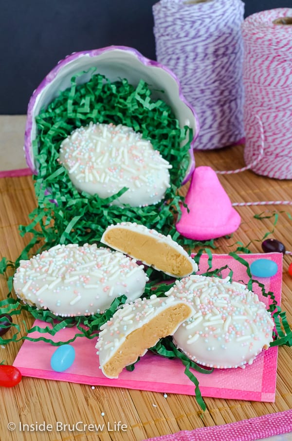 A pink napkin with green Easter grass and white chocolate cookie butter eggs and candies on it