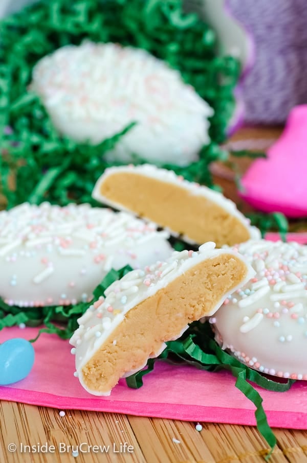 A pink napkin with green Easter grass on it and white chocolate cookie butter eggs stacked on it with one cut in half showing the filling