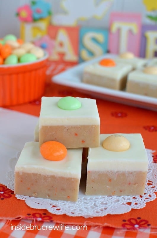 Carrot cake fudge topped with a cream cheese fudge stacked together on a white doily.