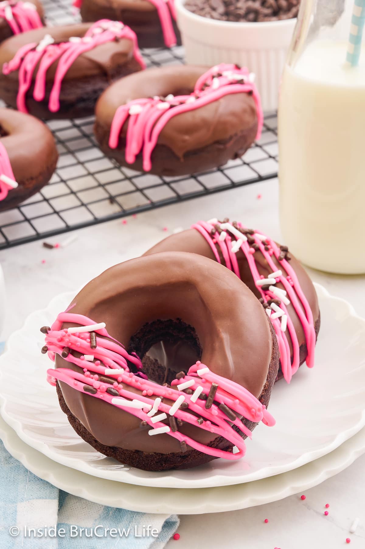 Two chocolate glazed donuts with sprinkles on a white plate.