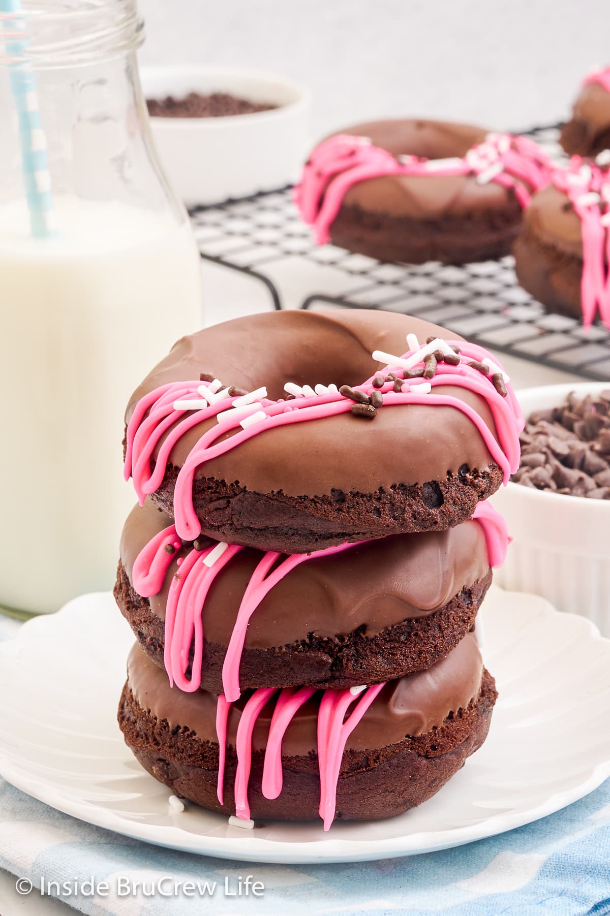 A stack of three chocolate donuts with chocolate and sprinkles on top.