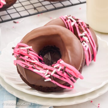 Two chocolate glazed donuts with sprinkles on a white plate.
