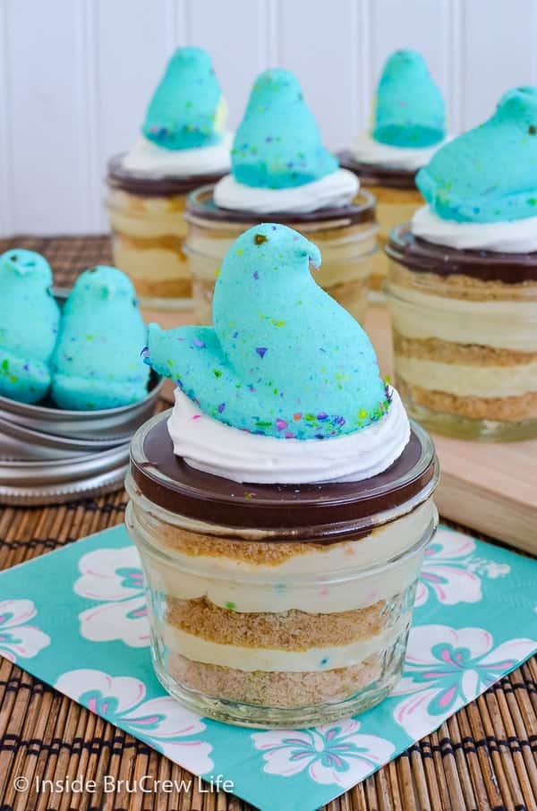 A jar of funfetti eclair cake with a blue marshmallow Peep on top and more jars behind it