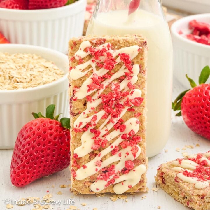 A strawberry topped granola bar standing next to a glass of milk.