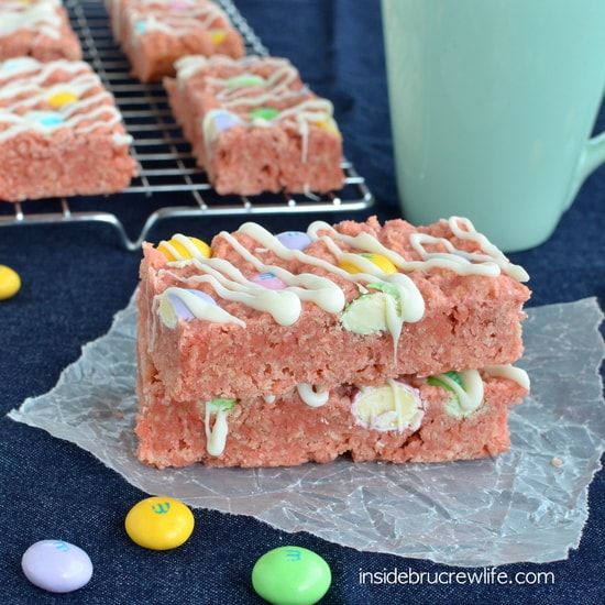 Two strawberry granola bars topped with white chocolate and M&M's on wax paper