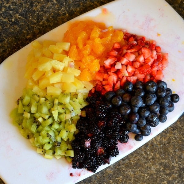 Six different fruits cut and arranged in circle on a white cutting board