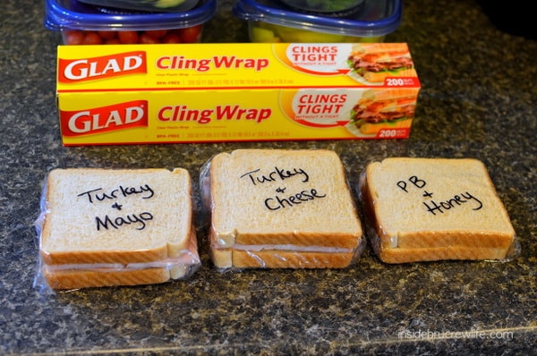 Three labeled sandwiches wrapped in plastic wrap