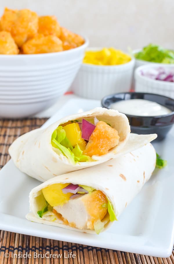 A white plate with a mango chicken wrap cut in half and propped up on its side