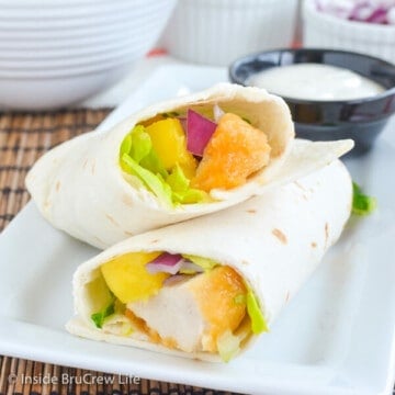 A white plate with a mango chicken wrap cut in half on it