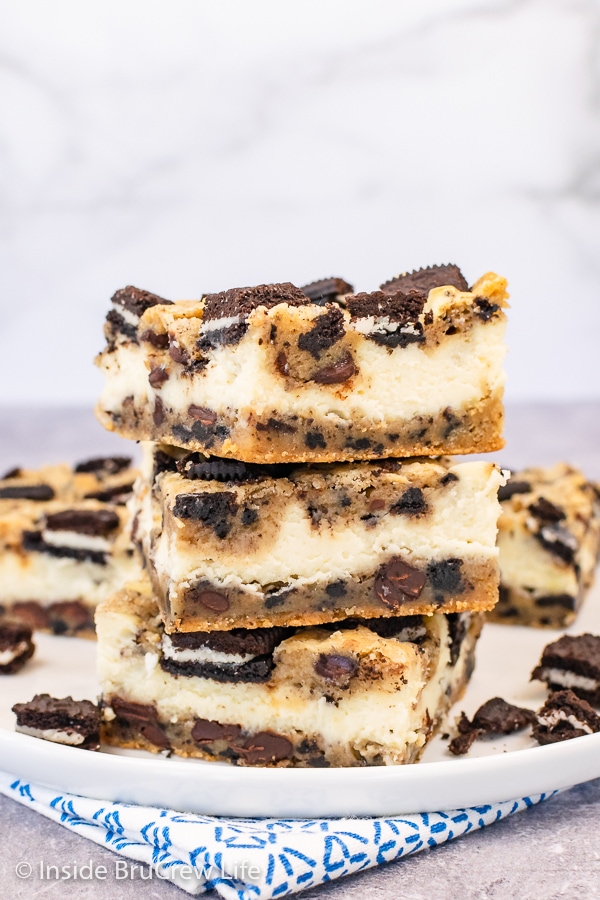 Three chocolate chip cheesecake bars stacked on top of each other on a white plate.