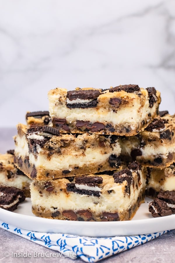 A white plate with squares of Oreo chocolate chip cheesecake bars stacked on it.