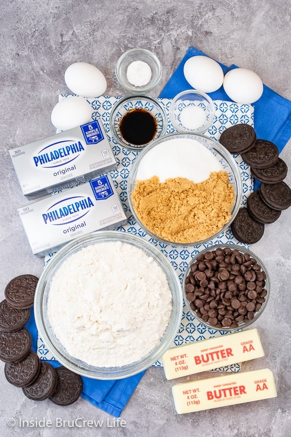 Bowls of ingredients to make cheesecake cookie bars on a gray board.