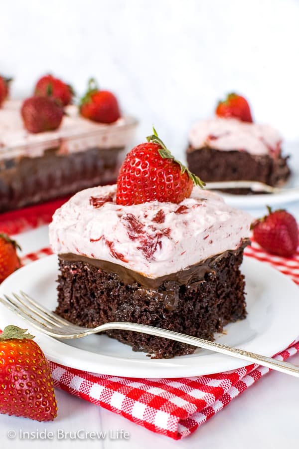 A white plate with a piece of strawberry fudge poke cake on it and the rest of the cake behind it