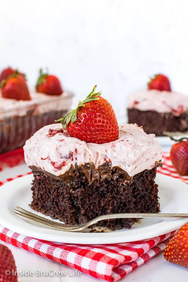 A white plate with a piece of strawberry fudge poke cake on it with a bite missing in the front of the cake