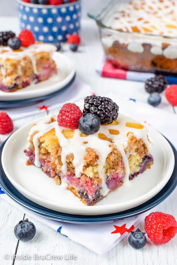 A square of triple berry coffee cake topped with glaze and fresh berries on a white plate
