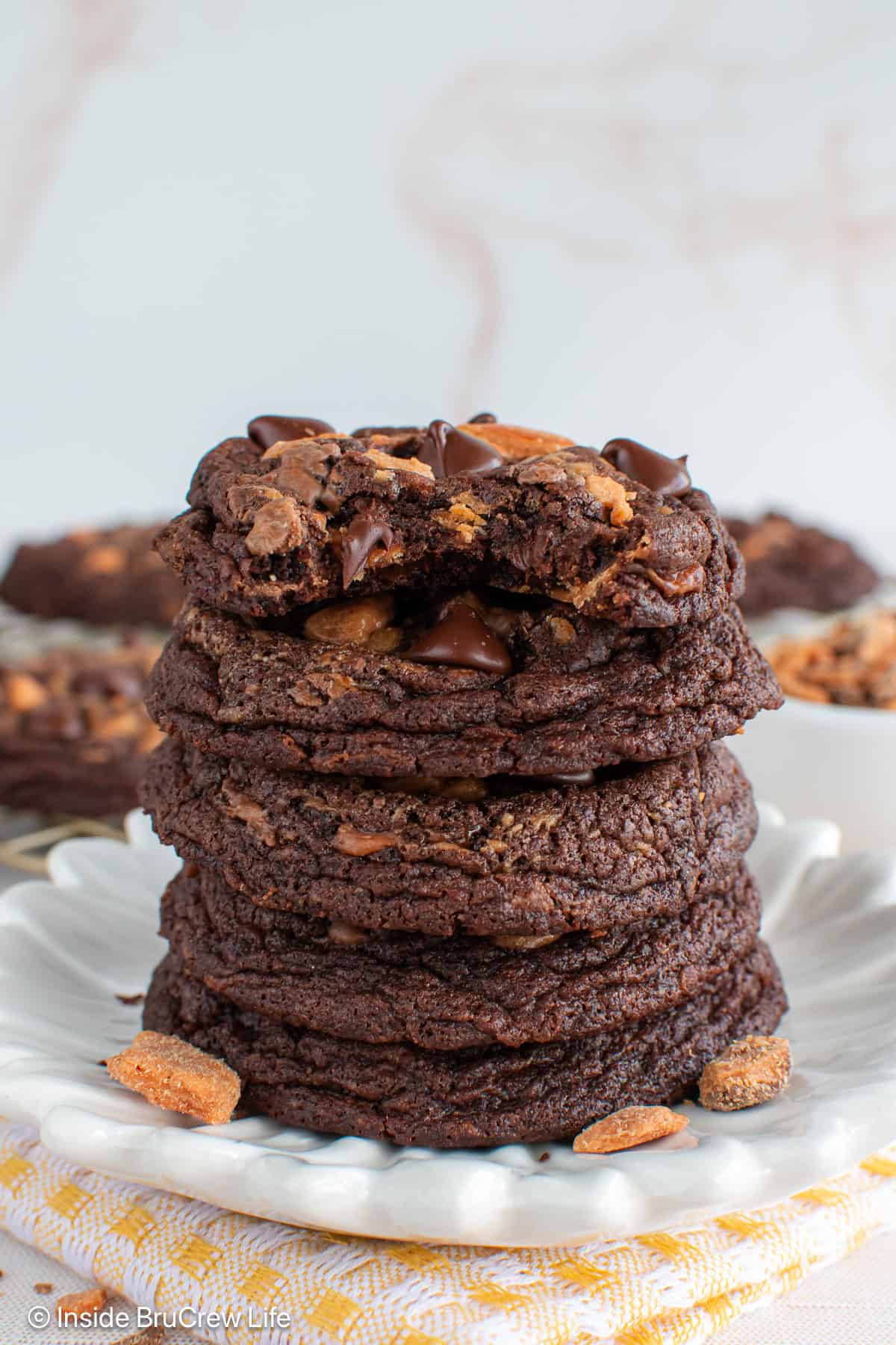 A stack of dark chocolate Butterfinger cookies on a white plate with a bite out of the top one.