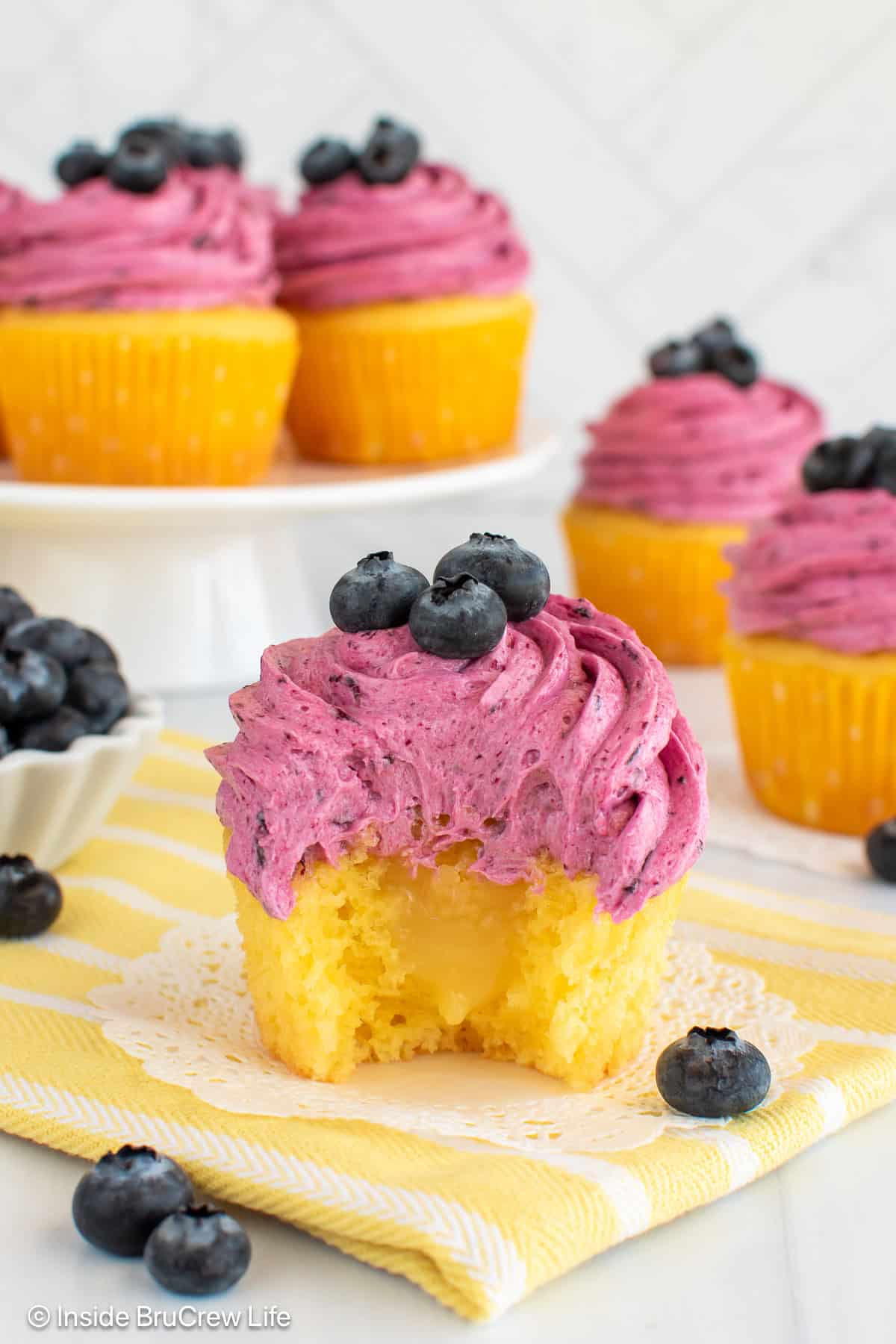 A lemon cupcake with blueberry frosting with a bite out of it showing a lemon curd center.