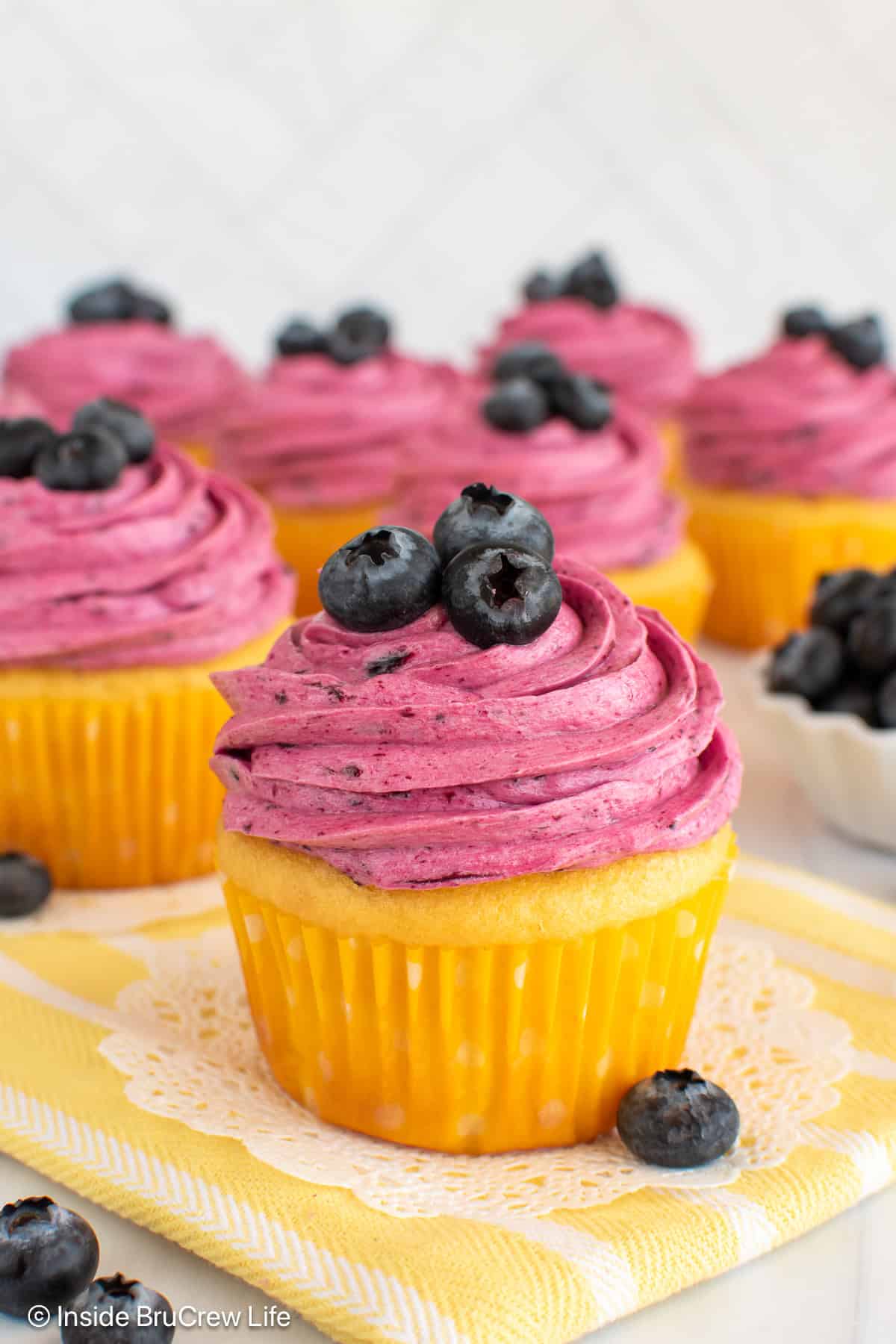 Lemon blueberry cupcakes on a yellow towel.