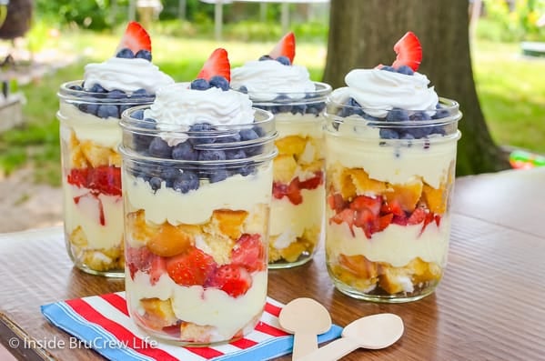 Four Lemon Fruit Parfaits with layers of cake, lemon mousse, and berries on a table outside