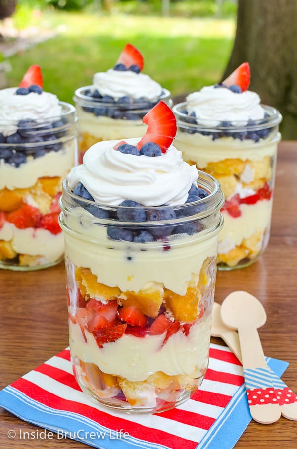 Jars with layers of snack cakes, lemon mousse, and fresh fruit on a table outside