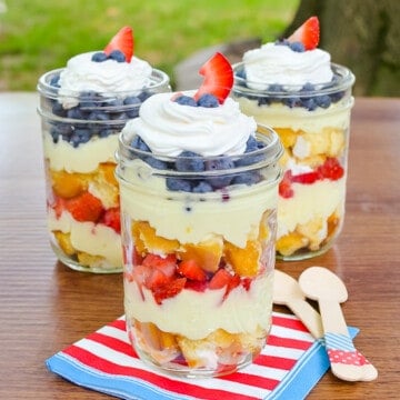 Three Lemon Fruit Parfaits on a table outside with layers of fruit, cake, and lemon mousse