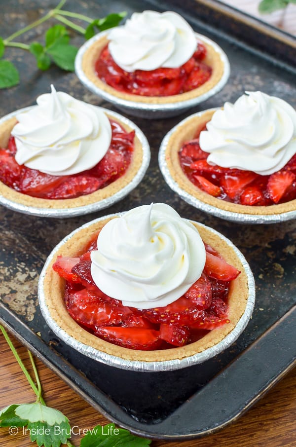 A black metal baking sheet with four no bake strawberry pies topped with whipped cream on it