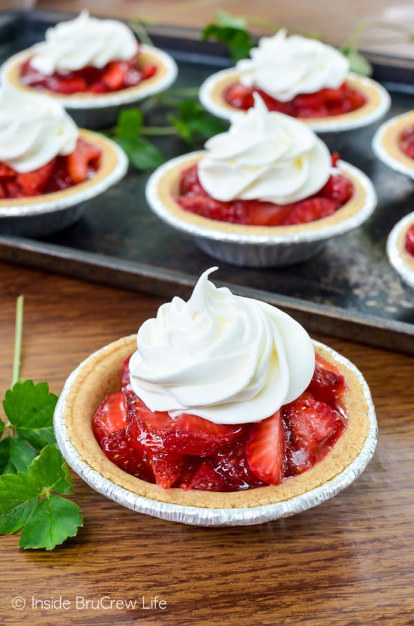 A mini strawberry pie topped with Cool Whip on a table with a tray of pies behind it