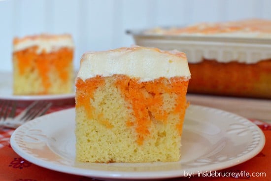 A square of orange poke cake with vanilla pudding frosting on it
