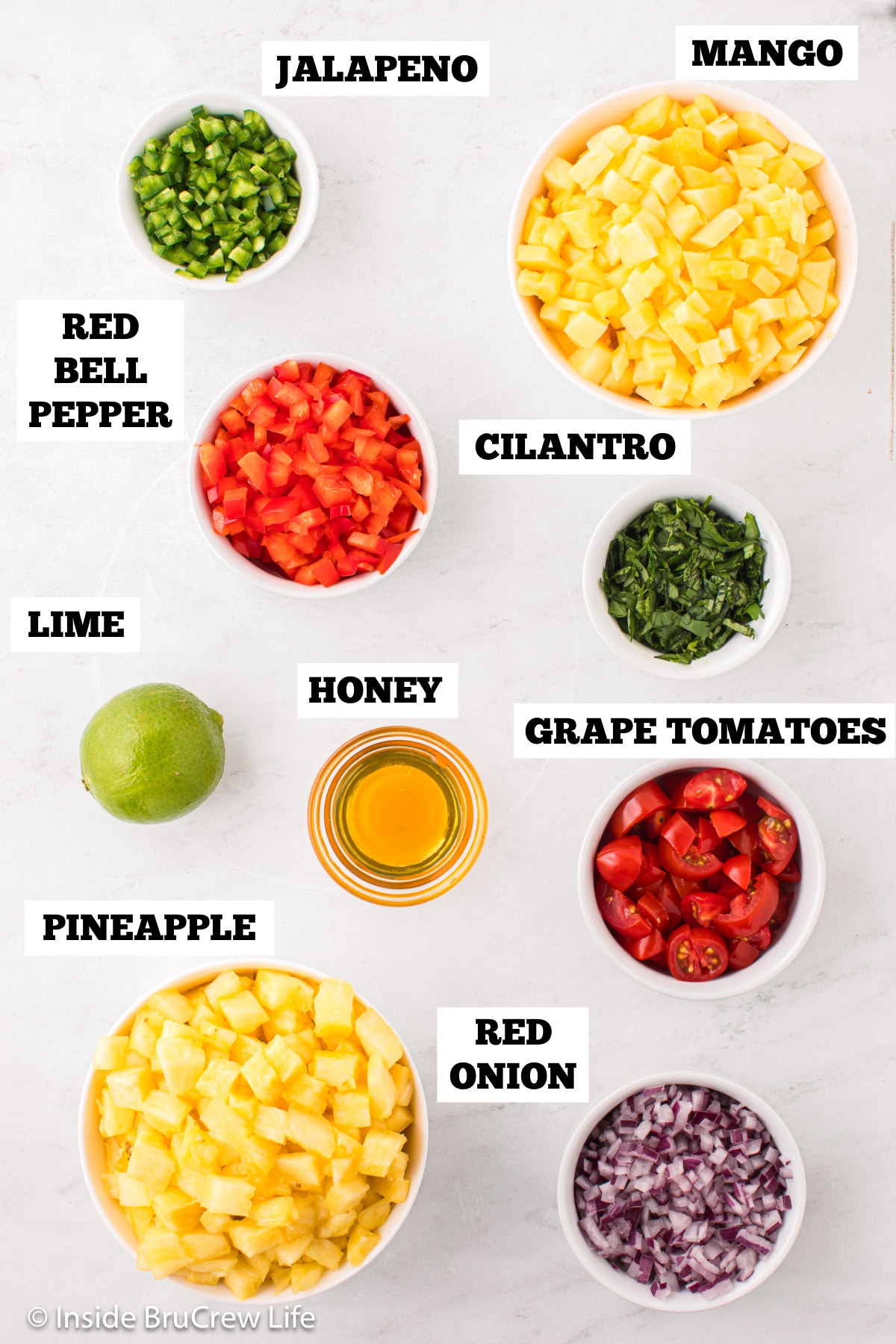 A white board with bowls of ingredients to make salsa with fruit.