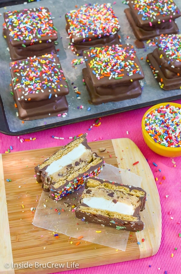 A wood tray with a no bake cookie dough s'mores cut in half and facing upward and more s'mores behind it