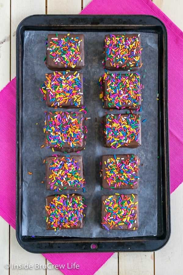 A metal tray with sheet of wax paper and 10 no bake cookie dough s'mores with colorful sprinkles on top of it