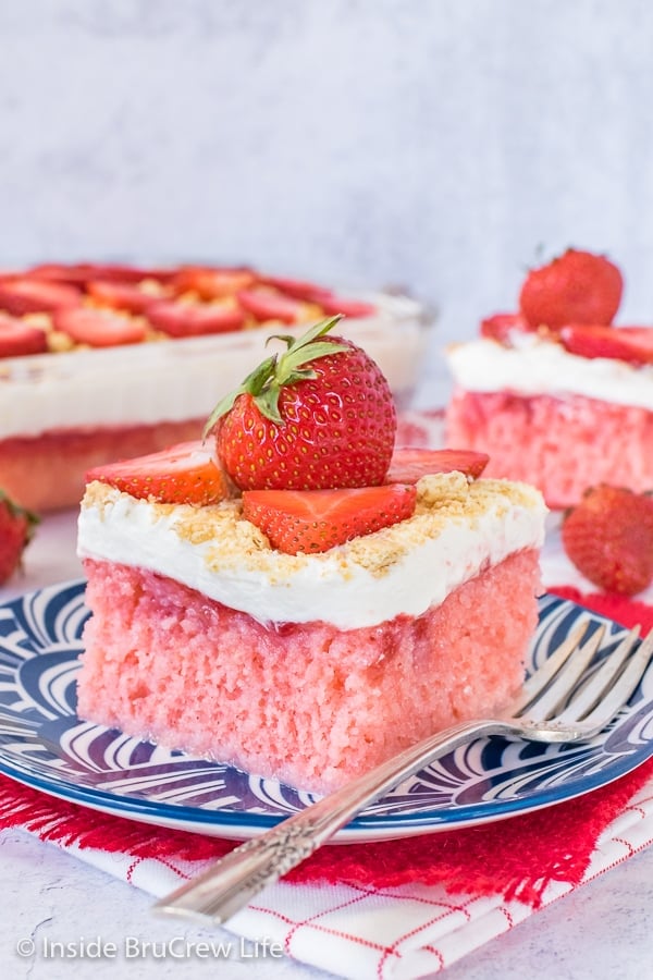 A blue plate with a piece of strawberry cheesecake poke cake and a fork on it.