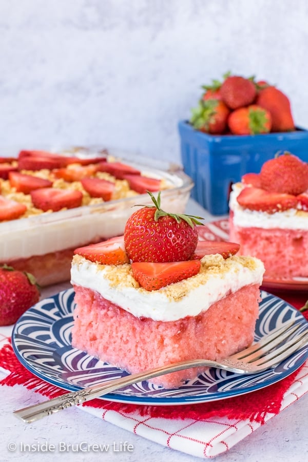 A piece of strawberry cheesecake poke cake on a blue plate with more cake behind it.