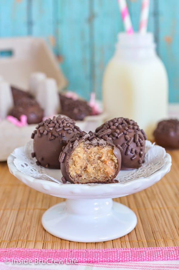 A little white cake stand with three butterfinger cookie dough truffles on it with a bite out of the front one