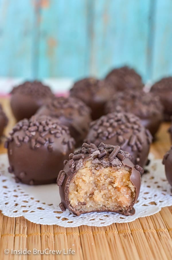 Lots of chocolate covered butterfinger cookie dough truffles with chocolate sprinkles on a yellow wood placemat