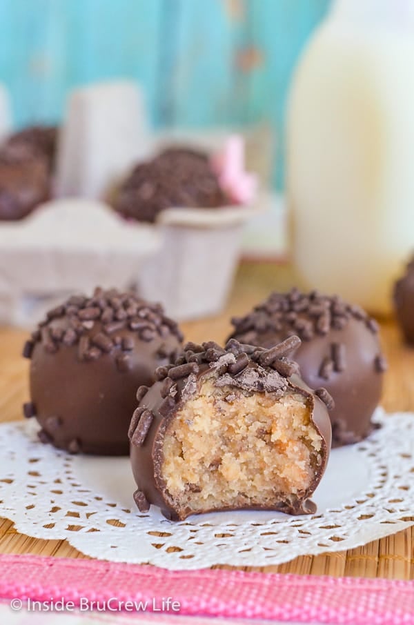 Three butterfinger cookie dough truffles on a white doily with a bite taken out of the front one