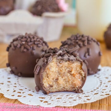 Three chocolate covered butterfinger cookie dough bites on a white doily with a bite out of the front truffle