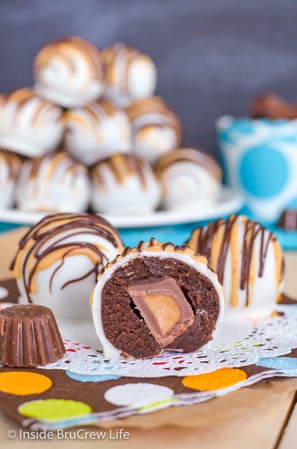 Three chocolate cookie dough truffles dipped in white chocolate with chocolate and peanut butter drizzles. One truffle cut in half showing the candy inside.