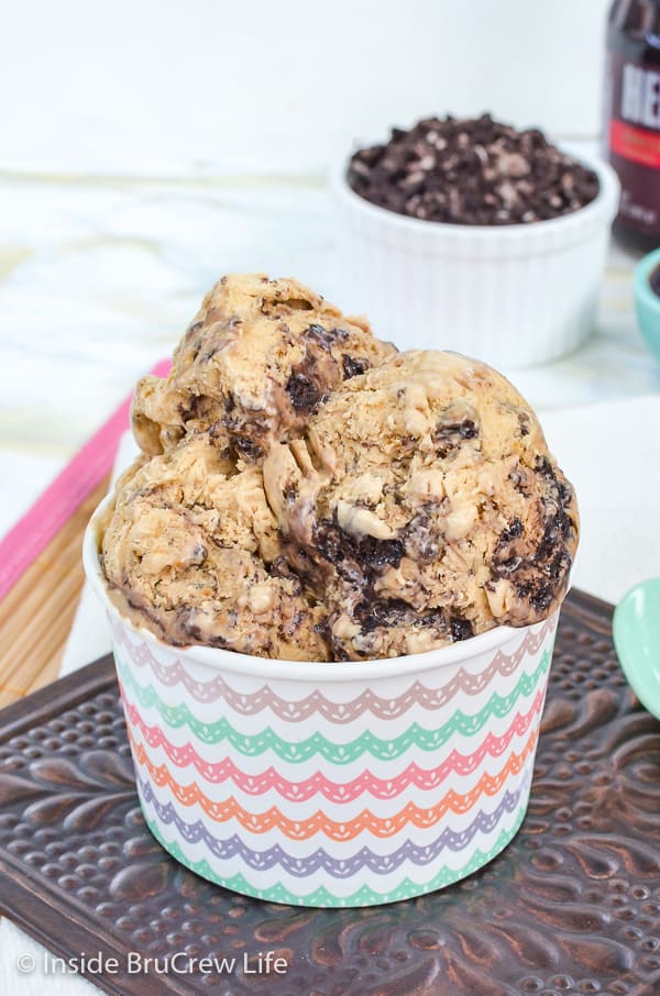 A white paper bowl filled with oreo fudge cappuccino ice cream and a bowl of oreo chunks behind it