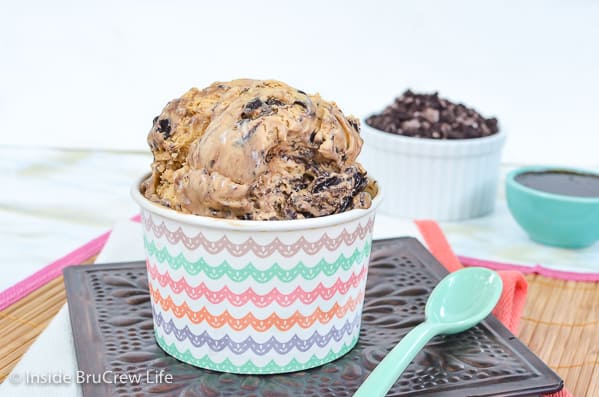 A white bowl with colorful lines filled with oreo fudge cappuccino ice cream and bowls of Oreo cookies and hot fudge behind it