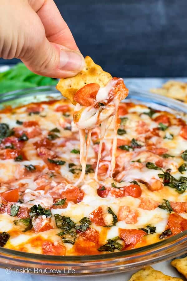 A clear pan full of cheesy dip with a cracker being dipped in it.