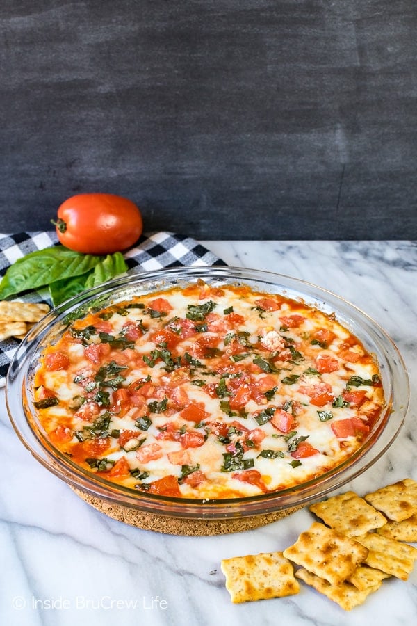 A glass pie pan full of pizza dip with tomatoes and basil on top.