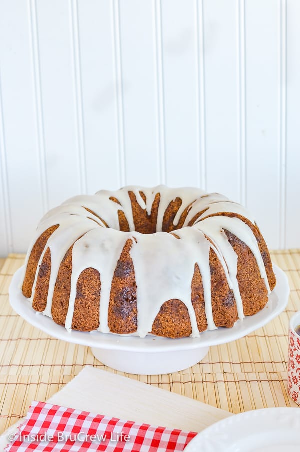 A white cake plate with a glazed apple bundt cake on it.