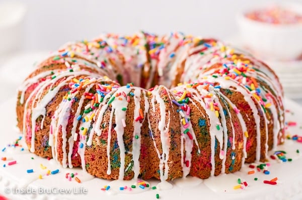 A full bundt cake topped with white glaze and lots of rainbow sprinkles.