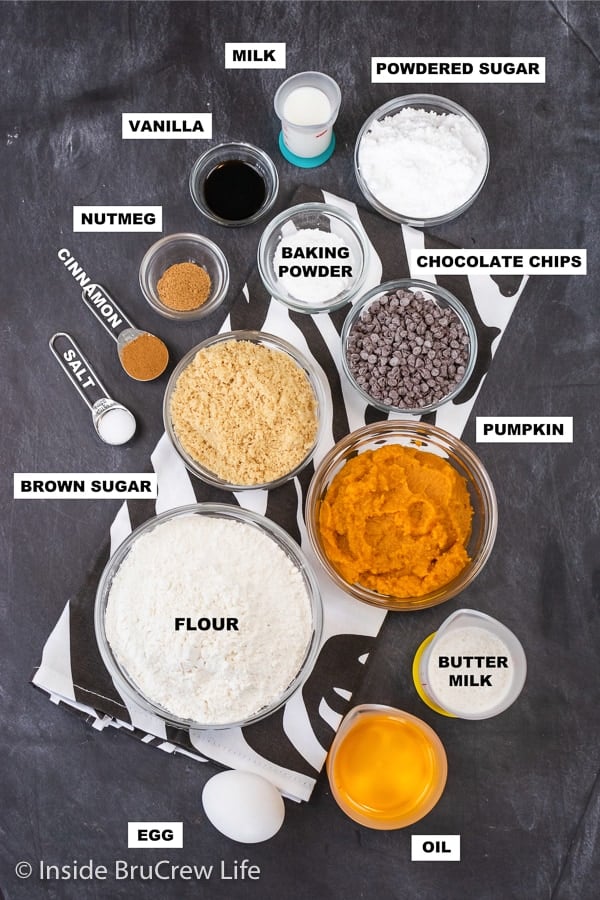 A dark board with bowls of ingredients needed to make mini pumpkin muffins with chocolate chips.