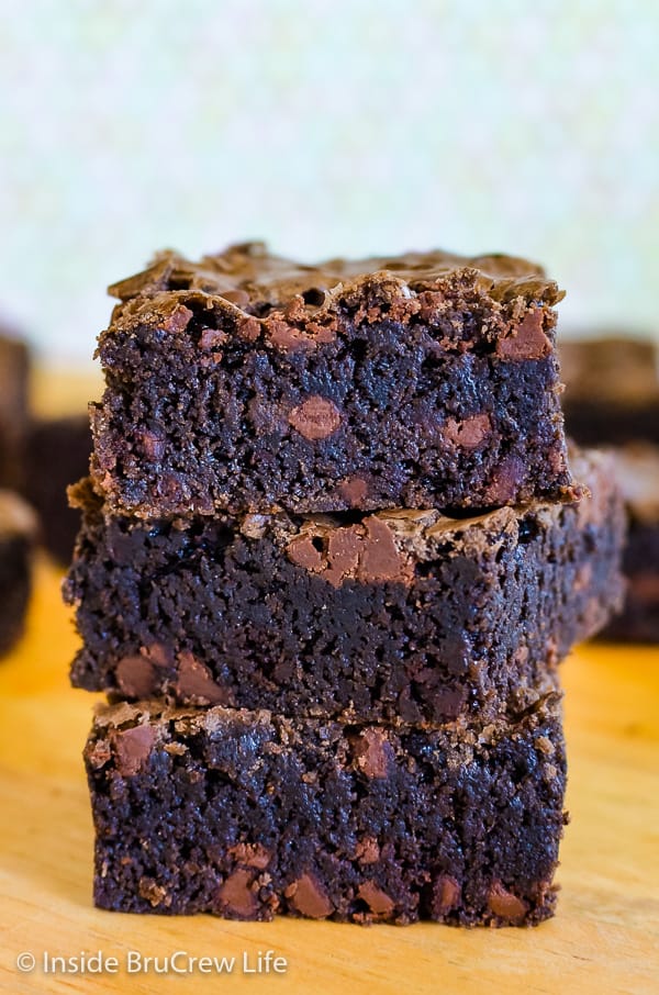 Three homemade brownies with chocolate chips stacked on a cutting board.