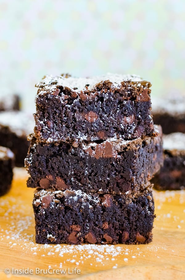 Three homemade brownies with chocolate chips stacked on top of each other and sprinkled with powdered sugar.