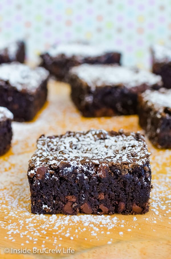 A cutting board with squares of homemade brownies sprinkled with powdered sugar on it